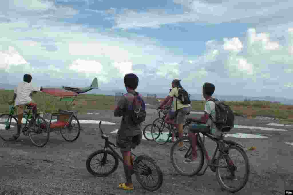 Children on bicycles watch a military cargo plane ferrying aid take off from Tacloban airport, Nov. 21, 2013. (Steve Herman/VOA)