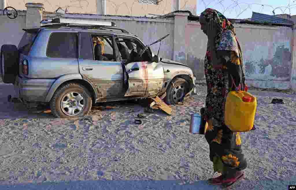 Seorang perempuan Somalia melewati rongsokan mobil yang baru saja meledak akibat bom di Mogadishu.