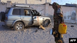 Sorang perempuan Somalia melewati mobil yang terkena serangan bom di Mogadishu (27/11). (AFP/Mohamed Abdiwahab)