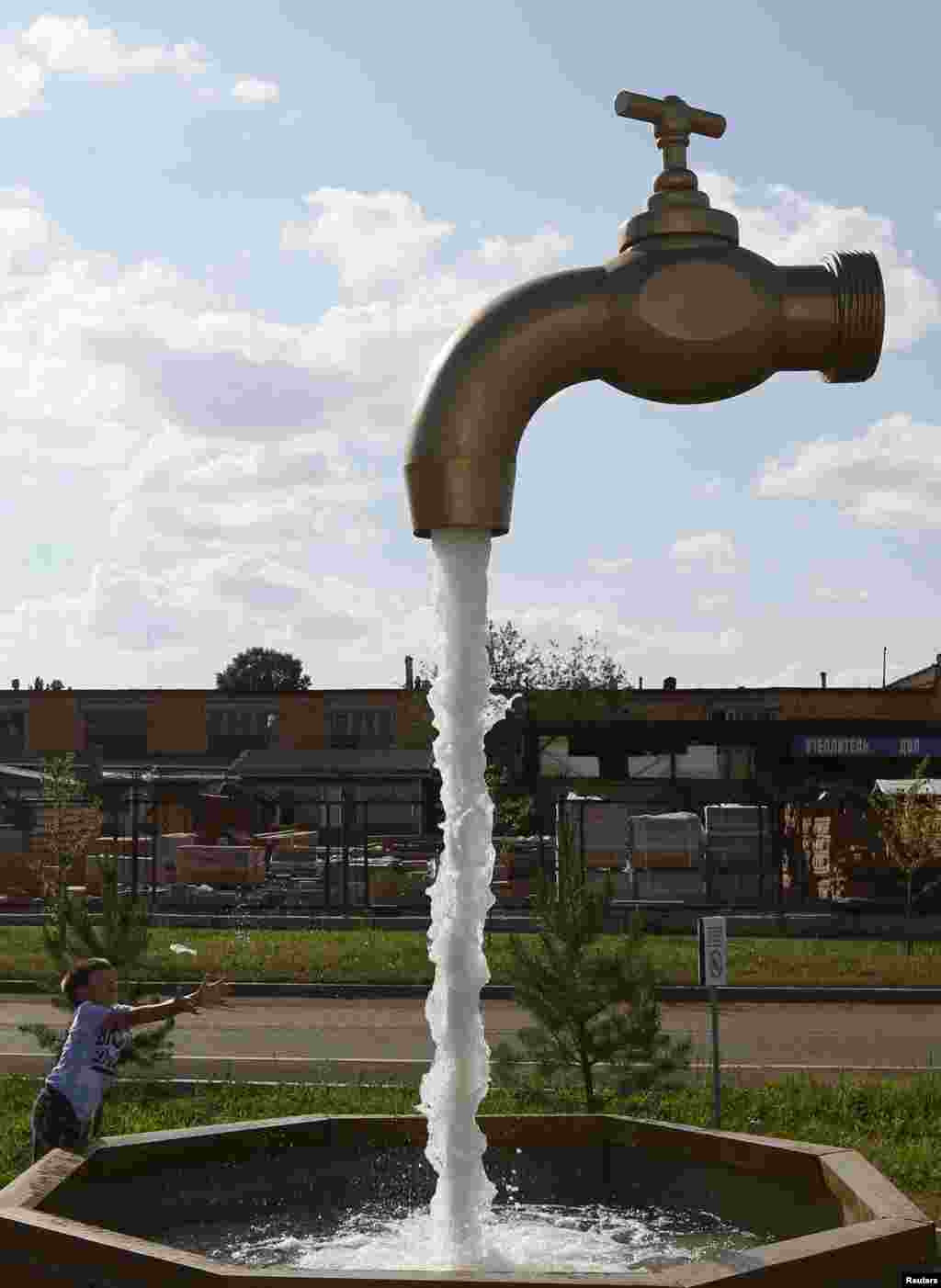 A boy plays near a fountain depicting a water tap in the Siberian city of Krasnoyarsk, Russia, July 27, 2015.