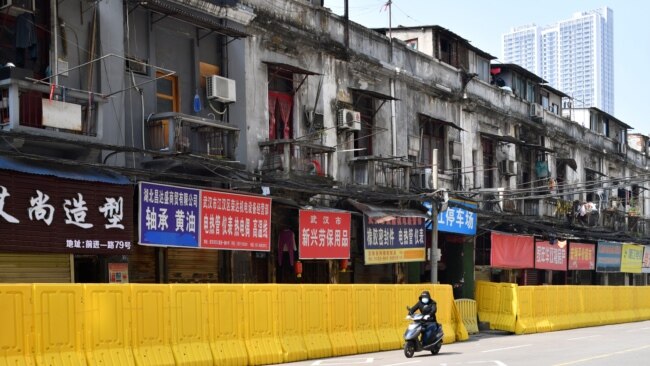 一名戴着口罩的骑车男子在武汉街头被封堵的商店旁驶过。（2020年3月5日）