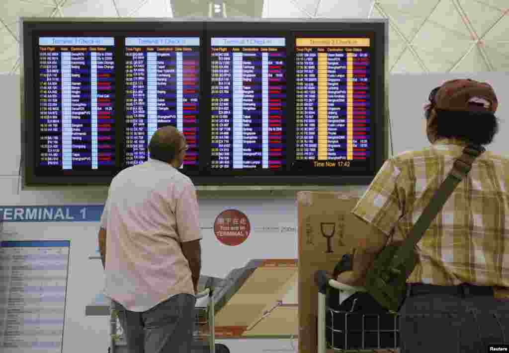 Passengers look at an information board which shows nearly all departure flights were cancelled, in anticipation of Typhoon Usagi, at Hong Kong Airport, Sept. 22, 2013.