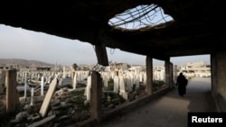 FILE - A woman walks at a cemetery in Douma, in the eastern suburbs of Damascus, Syria, March 9, 2021.