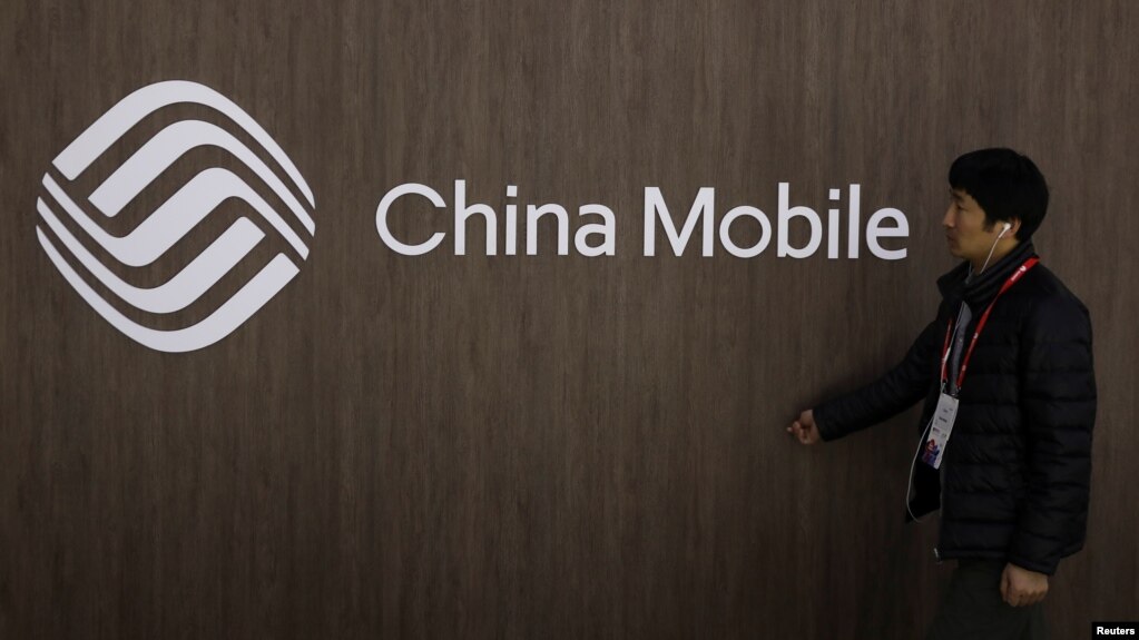 Một người đàn ông đi ngang qua logo của hãng China Mobile. 