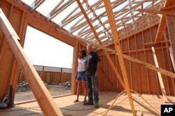 In this Aug. 9, 2018 photo, Cheri and Paul Sharp stand among the wooden beams framing their future home in Santa Rosa, Calif.