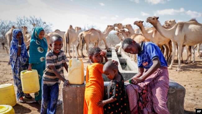 FILE - Herder children who look after their family's camels cool off and fill plastic containers with water from a water point in the desert near Dertu, Wajir County, Kenya, Oct. 24, 2021.