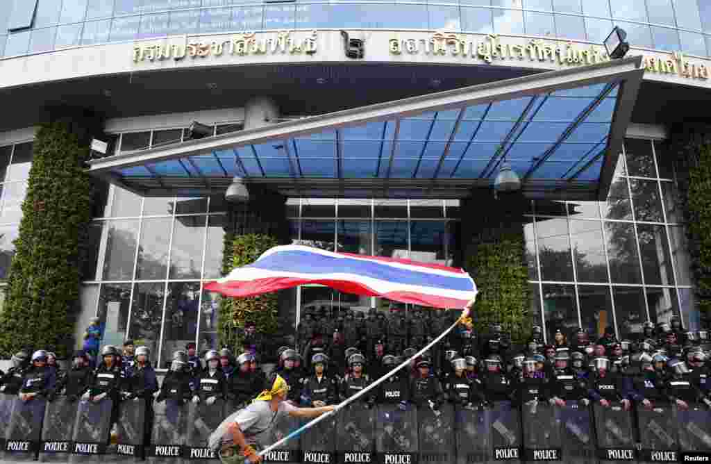 An anti-government protester waves a national flag in front of riot police officers and soldiers guarding the entrance of the National Broadcast Services of Thailand (NBT) television station, in Bangkok, May 9, 2014.