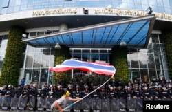 在位于曼谷的泰国全国广播服务电视台大楼前，一名反政府抗议人士在镇暴警察前挥舞国旗。 （2014年5月9日）