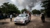 Un véhicule de campagne passe non loin de la fumée d'un incendie dans l'entrepôt de la Commission électorale nationale indépendante (CENI), dix jours avant les élections, à Kinshasa le 13 décembre 2018.