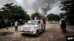 Un véhicule de campagne passe non loin de la fumée d'un incendie dans l'entrepôt de la Commission électorale nationale indépendante (CENI), dix jours avant les élections, à Kinshasa le 13 décembre 2018.