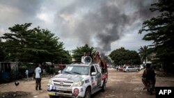 Un véhicule de campagne passe non loin de la fumée d'un incendie dans l'entrepôt de la Commission électorale nationale indépendante (CENI), dix jours avant les élections, à Kinshasa le 13 décembre 2018.