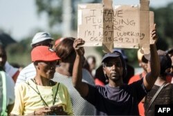 FILE - An unemployed man holds up a sign as the South African president begins his address at the Sugar Ray Xulu stadium in Clermont township, north of Durban, May 1, 2019.