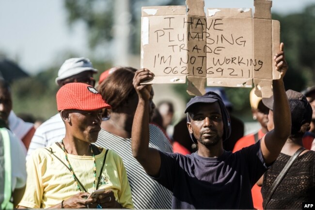 FILE - An unemployed man holds up a sign as the South African president begins his address at the Sugar Ray Xulu stadium in Clermont township, north of Durban, May 1, 2019.