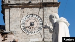 在意大利古镇诺尔恰，一座圣本笃像指向在地震中受损的市政厅的大钟。（2016年10月31日）