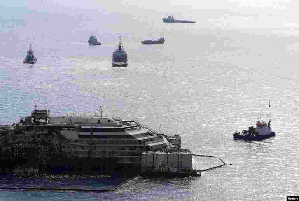 The Costa Concordia is surrounded by tugboats as it begins its journey to Genoa for dismantling, from Giglio harbour at Giglio Island, July 14, 2014.