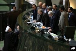 Iranian President Hassan Rouhani, left, presents a draft of the country's new budget and sixth development plan to the parliament speaker Ali Larijani in an open session of parliament, in Tehran, Iran, Jan. 17, 2016.