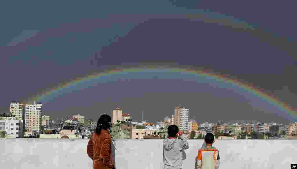 Palestinian children look at a rainbow shining over buildings after heavy rain poured in Gaza City, Gaza.