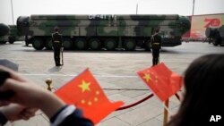 FILE - Onlookers wave Chinese flags as military vehicles carrying DF-41 ballistic missiles pass during a parade in Beijing, China, Oct. 1, 2019.