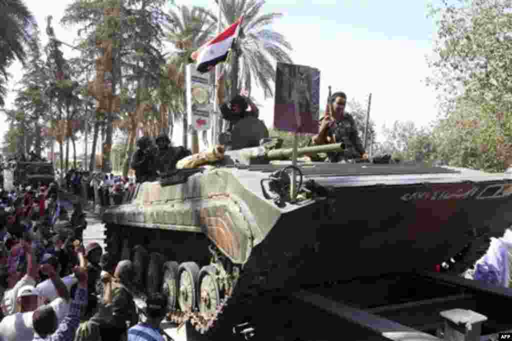 In this photo taken on a government-organized tour, Syrian soldiers salute residents as they sit atop their armored personnel carrier on their way out of the eastern city of Deir el-Zour, Syria, Tuesday, Aug. 16, 2011. State-run news agency SANA said army