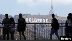 FILE - Tourists walk past the Hollywood sign as they visit a shopping complex along Hollywood Boulevard in Hollywood, California, Aug. 3, 2017.