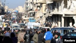 Rebel fighters and civilians wait near damaged buildings to be evacuated from a rebel-held sector of eastern Aleppo, Dec. 18, 2016.