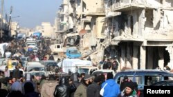 FILE - Rebel fighters and civilians wait near damaged buildings to be evacuated from a rebel-held sector of eastern Aleppo, Dec. 18, 2016. 