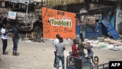 Des gens se tiennent près d'un mur d'une boutique endommagée qui dit: "non à la violence, Toumodi est la base" sur le marché de Toumodi le 4 novembre 2020.