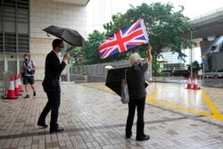 Seorang aktivis pro-demokrasi memegang bendera Inggris ketika para aktivis pro-demokrasi yang dituduh melakukan subversi tiba di pengadilan Hong Kong, 23 September 2021.