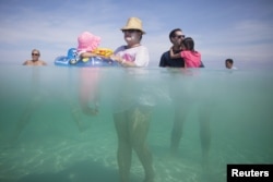 FILE - Retiree Madeline Barcelo (C) holds her granddaughter surrounded by relatives at the beach in Varadero, Cuba, Aug. 26, 2015.
