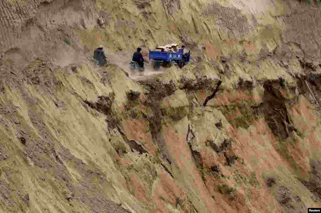 Dua sepeda motor dan sebuah truk berjalan dekat tebing dari sebuah kawasan yang mengalami longsor setelah gempa 6,6 skala Richter di Minxian, provinsi Gansu, China.