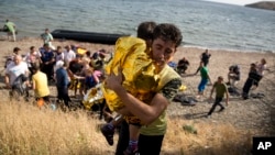 A Syrian man carries a child wrapped in a thermal blanket as they arrive with others at the coast on a dinghy after crossing from Turkey, at the island of Lesbos, Greece, Sept. 7, 2015. 