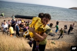 A Syrian man carries a child wrapped in a thermal blanket as they arrive with others at the coast on a dinghy after crossing from Turkey, at the island of Lesbos, Greece, Sept. 7, 2015.