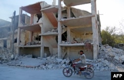 FILE - A Syrian man rides a motorcycle past a destroyed building in an area that was hit by a reported airstrike in the district of Jisr al-Shughur, in the Idlib province, Sept. 4, 2018.
