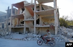 A Syrian man rides a motorcycle past a destroyed building in an area that was hit by a reported airstrike in the district of Jisr al-Shughur, in the Idlib province, Sept. 4, 2018.