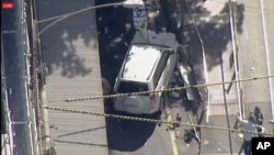 Foto tomada de un video de la televisión australiana que muestra un vehículo todoterreno blanco subido sobre la calzada en la calle Flinders, en el céntrico distrito de negocios de Melbourne.