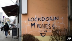 A pedestrian walks by grafitti reading "Lockdown Madness" in the district Schoeneberg in Berlin, Germany, March 23, 2021. 