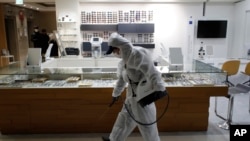 A worker wearing protective gear sprays disinfectant as a precaution against the new coronavirus in an eyeglass shop at a department store in Seoul, South Korea, March 2, 2020. 