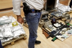 FILE - A member of Finance Crimes Squad stands in front of confiscated items after a news conference in Athens, , March 6, 2017.