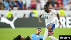 El delantero de Estados Unidos, Folarin Balogun (20), es derribado por el defensor uruguayo Ronald Araújo (4) durante la primera mitad de un partido de la Copa América en el Arrowhead Stadium.