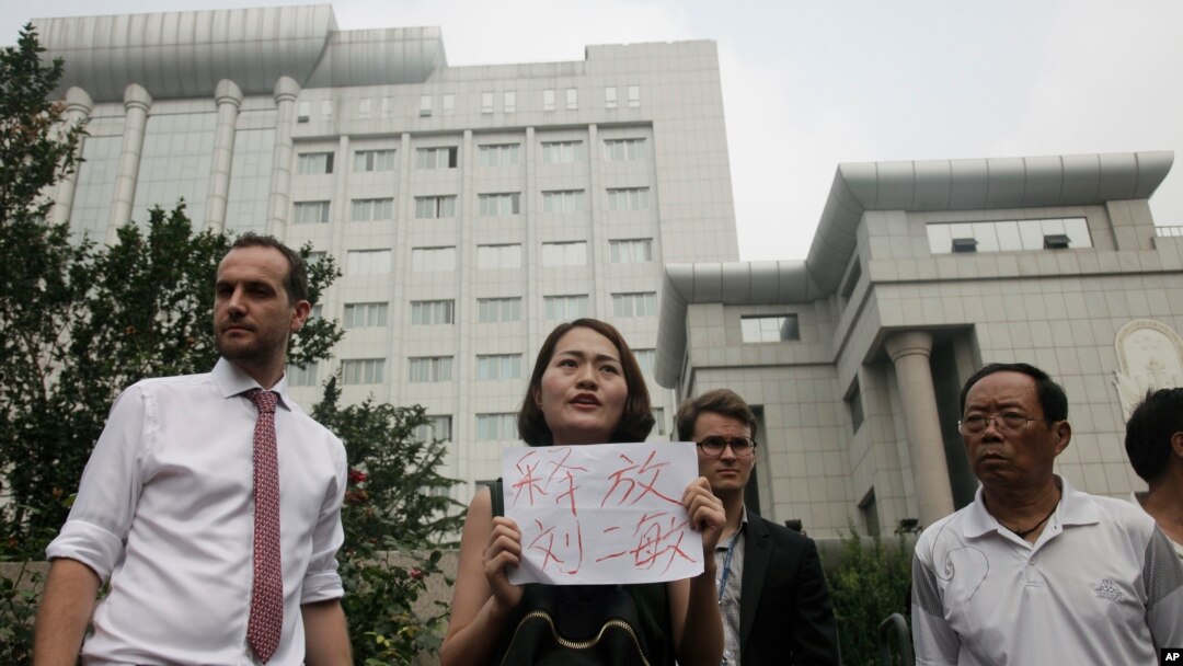 FILE - Li Wenzu, center, wife of imprisoned lawyer Wang Quanzhang, holds a paper that reads "Release Liu Ermin" as she and supporters of a prominent Chinese human rights lawyer and activists stage a protest outside the Tianjin No. 2 Intermediate People's Court.