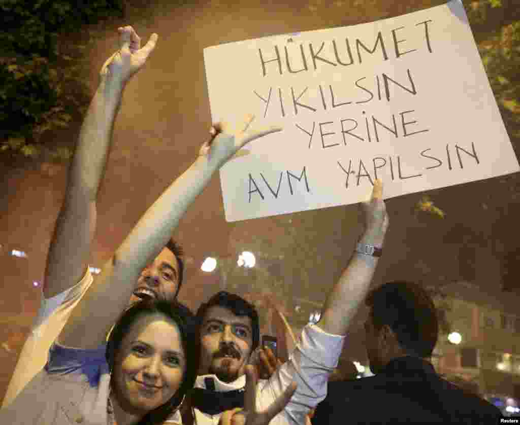 Protesters gesture as they hold a placard that reads 'Collapse the government and build a shopping mall in its place'', during clashes between police and anti-government protesters in Ankara, early, June 2, 2013.