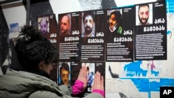 A woman hangs portraits of activists injured during protests against the government's decision to suspend negotiations on joining the European Union in Tbilisi, Georgia, on Dec. 7, 2024.