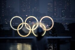 A woman walks past the Olympic rings lit up at dusk in the rain, on the Odaiba waterfront in Tokyo, July 9, 2021.