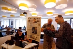 FILE - Journalists of the newspaper Nepszabadsag, which was shut down amid cries of a crackdown by Prime Minister Viktor Orban's government, paste a copy of its last issue onto a glass wall in a makeshift newsroom in Budapest, Hungary, Oct. 10, 2016.