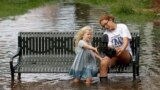 Katie Bender gets some assistance from Johanna Bender (L) as they dump water from a boot while sitting on a flooded street after Hurricane Arthur passed through in Manteo, N.C.