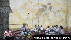 A man sits in front of a mural in Kuala Lumpur, Malaysia.