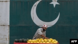 Seorang penjual buah mengenakan masker wajah sambil menunggu pembeli di Lahore, 9 April 2020. (Foto: AFP)