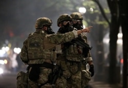 A federal law enforcement official points to demonstrators before firing tear gas during a protest against racial inequality in Portland, Oregon, July 19, 2020.