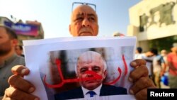 A protester holds a picture of Iraqi Prime Minister Haider al-Abadi with "Step Down" written on it during a protest at Tahrir square in Baghdad, Iraq, July 27, 2018. 