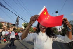 FILE - A woman holds a Chinese flag and stands by the side of a road to welcome Chinese President Xi Jinping in Kathmandu, Nepal, Oct. 12, 2019.